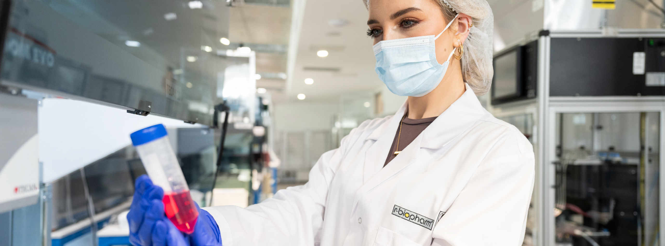 young woman in lab coat holding test tube with red liquid