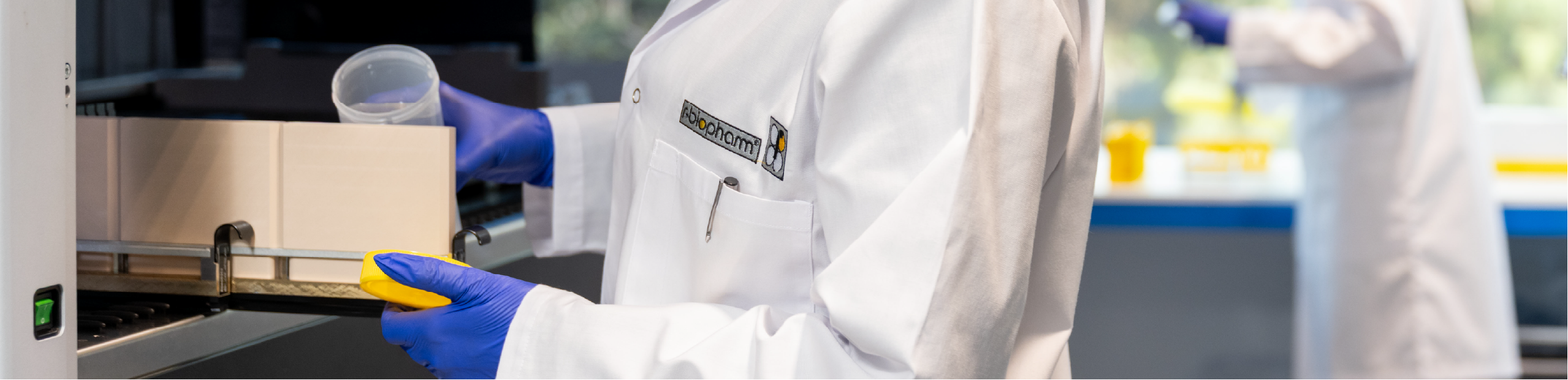 a woman in a lab coat prepares to place a vial of liquid into a machine to perform a medical diagnostic test