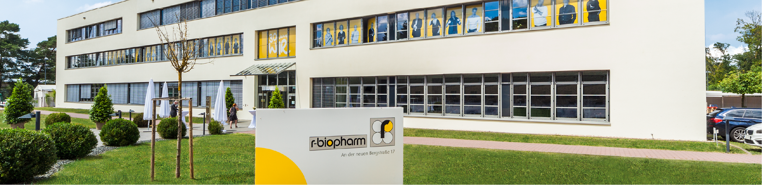 the exterior of an office building for R-Biopharm in Germany with a grey and yellow sign in the foreground on lush green grass