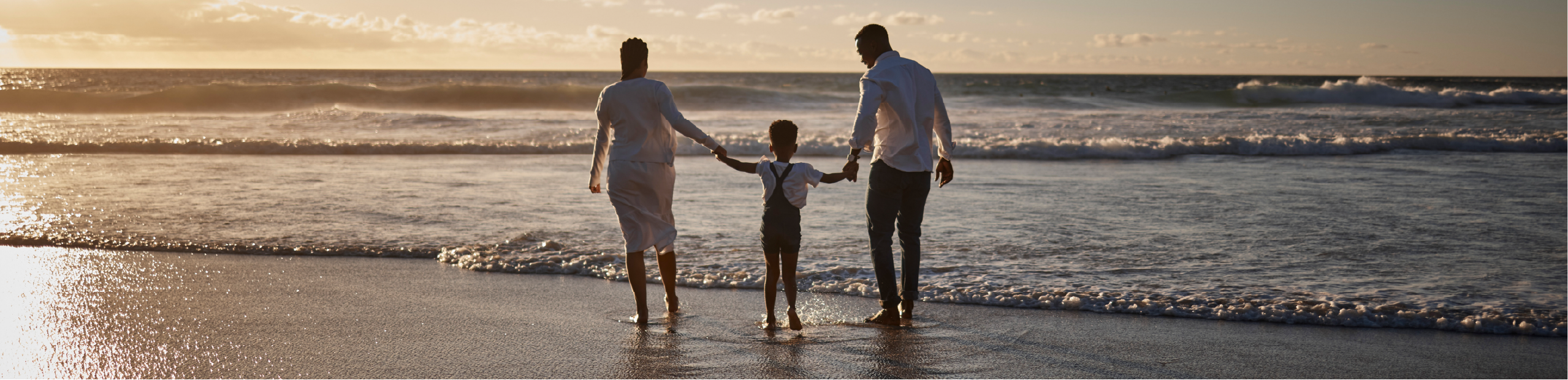 a young family walks hand-in-hand on a beach during sunset