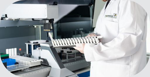 A man in a R-Biopharm branded lab coat holds a tray containing medical diagnostic equipment in front of a complex instrument designed to conduct medical diagnostic tests