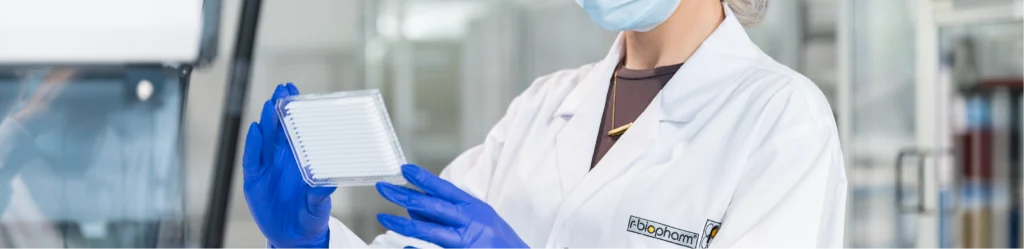 a woman in a facemask, lab coat and gloves holding medical diagnostic products