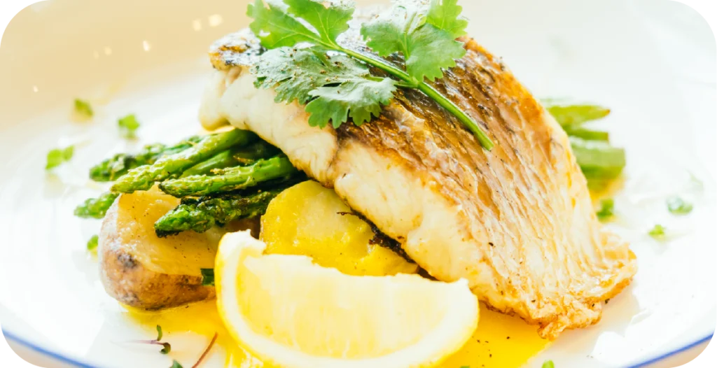 two fillets of cooked fish on a plate with fresh herbs and lemon wedges