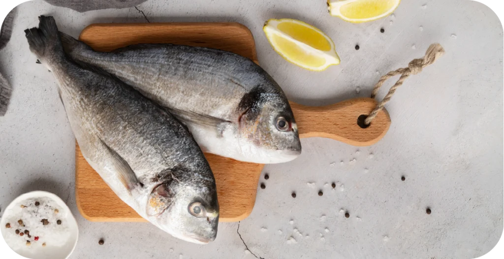two whole fish on a chopping board, surrounded by lemon and pepper