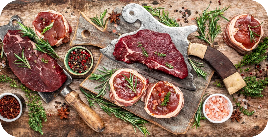 a series of steaks and other beef products sitting on a wooden board with an assortment of salts and peppercorns