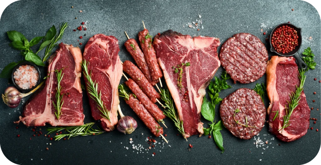 a series of raw meat products, including steaks, burger patties and kofta skewers arranged on a black table