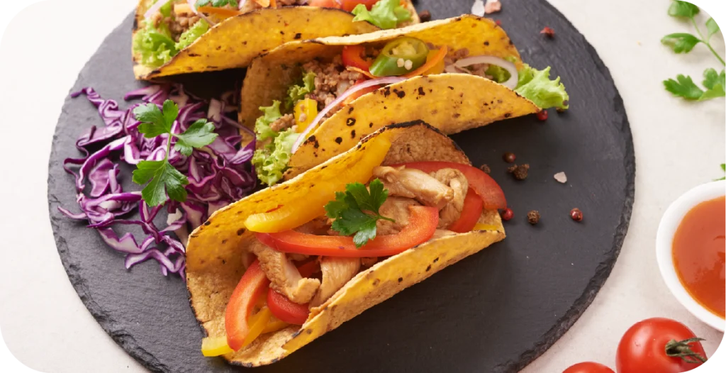 three corn tortilla based tacos on a black slate plate