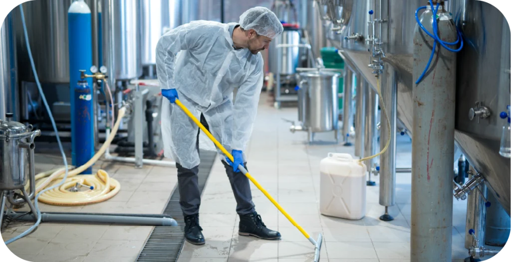 a man in PPE cleans the floor of a food processing plant with a mop and bucket