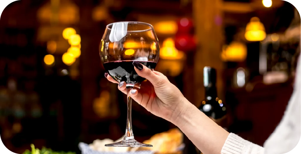a woman holds a glass of red wine up in a restaurant setting
