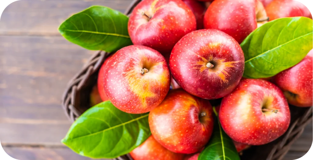 several red apples with green leaves in a bowl on a wooden table, ready for mycotoxin testing