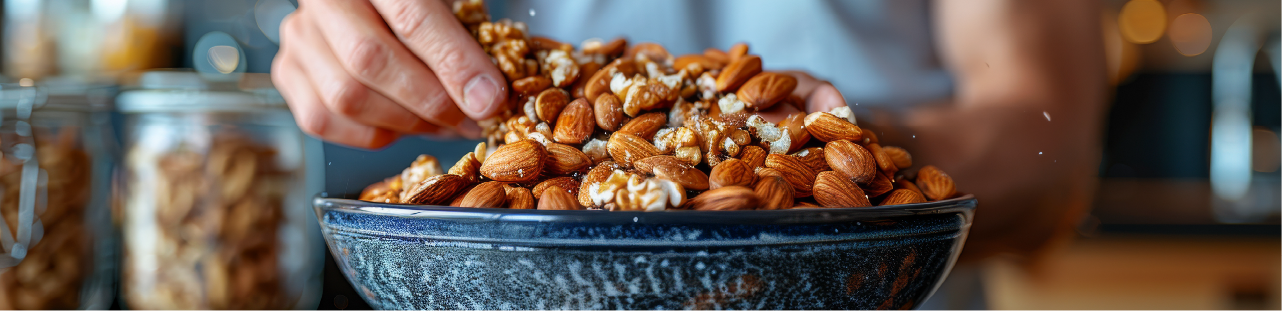 a man in a blue shirt picks a walnut out of a bowl filled with walnuts