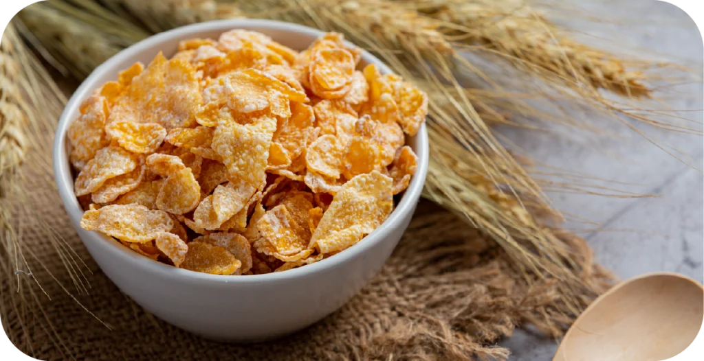 a bowl of corn flakes sits on a wooden board with an ear of wheat behind it