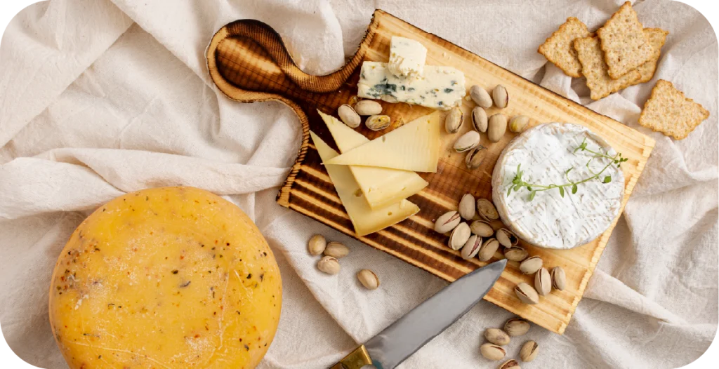 a series of cheeses, crackers and other goods on a wooden chopping board