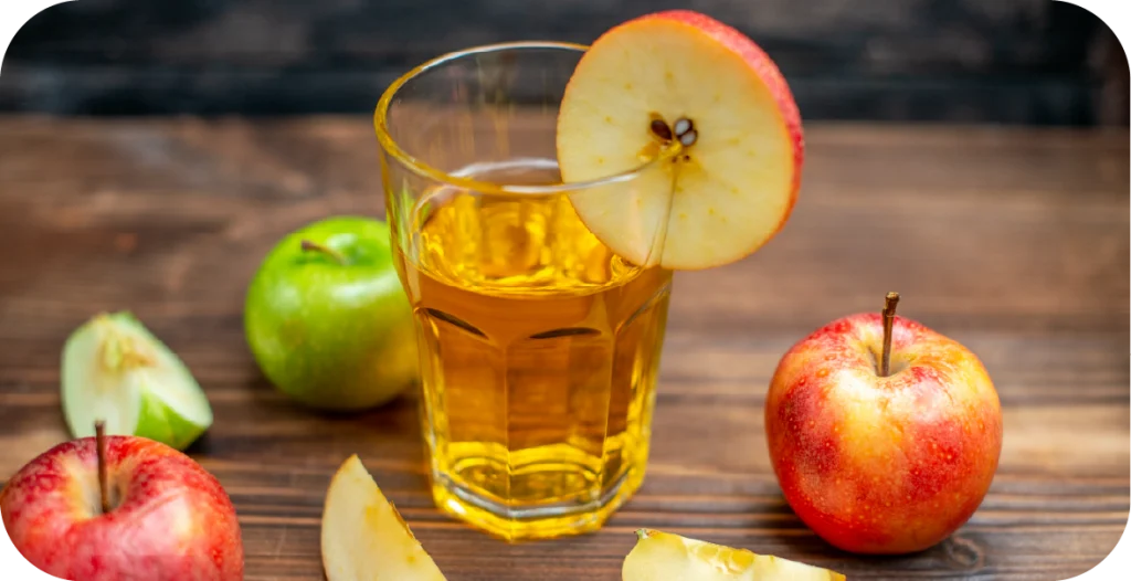 a glass of apple juice on a wooden table surrounded by whole apples and apple slices