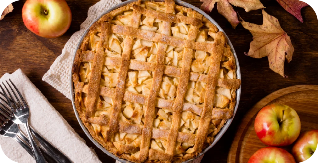 an apple pie sits on a table, surrounded by apples and cutlery. Apples should be subject to patulin testing