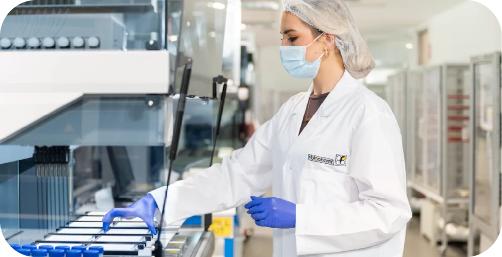 a young woman in a lab coat, hairnet and gloves places a tray of diagnostic testing products into a complex piece of machinery