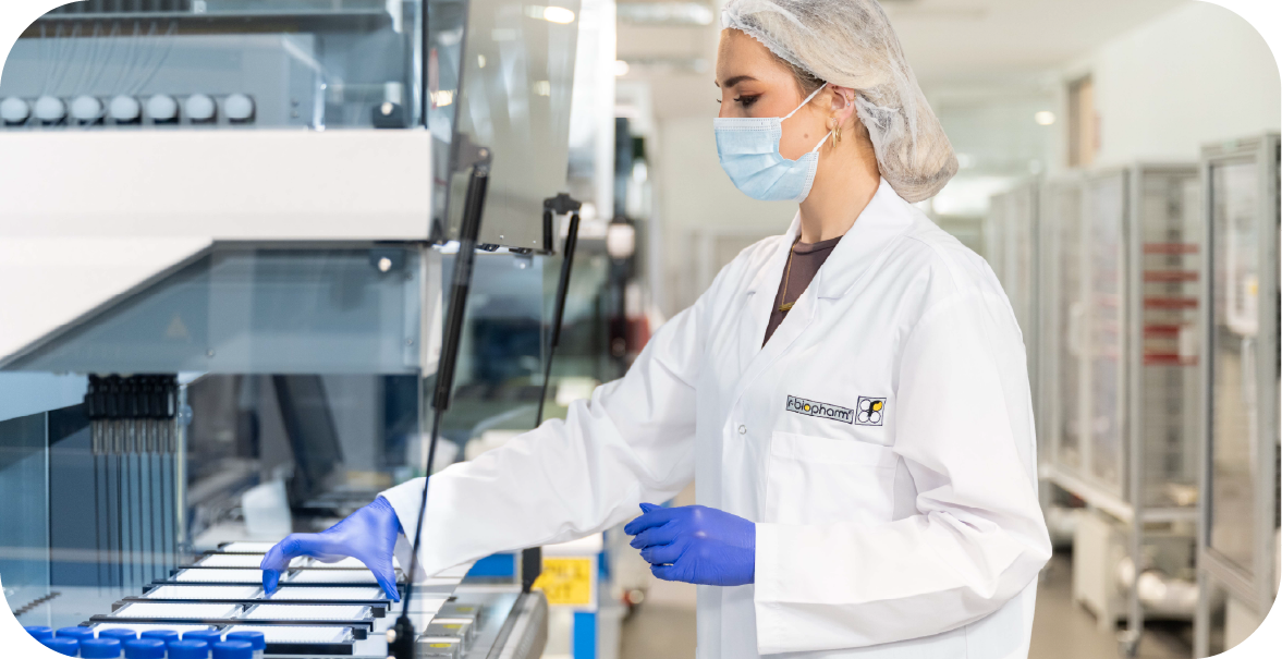 a young woman in a lab coat, hairnet and gloves places a tray of diagnostic testing products into a complex piece of machinery