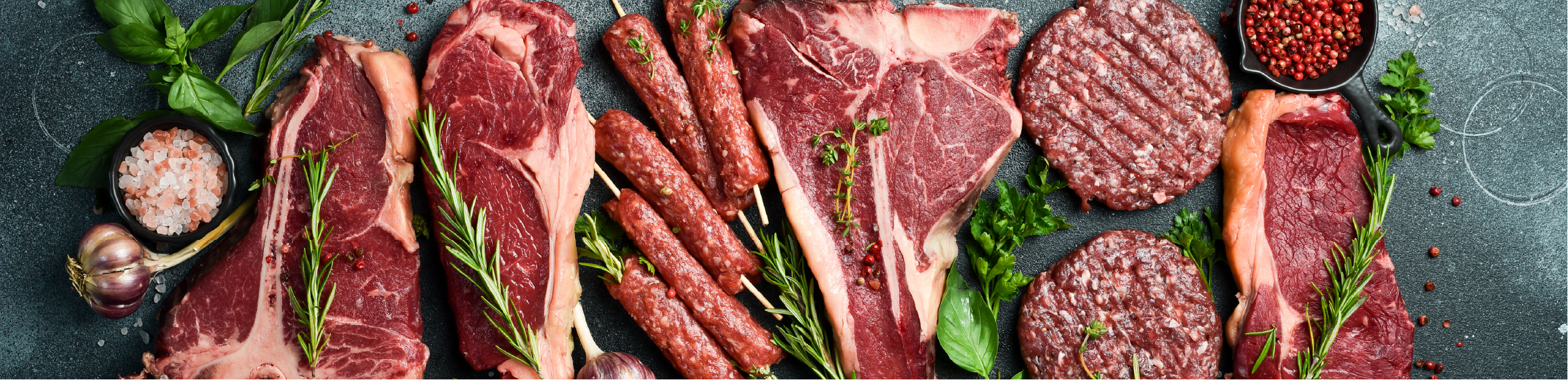 a series of raw meat products, including steaks, burger patties and kofta skewers arranged on a black table