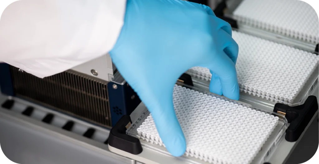 the arm of a scientist in a lab coat and a blue glove placing a plate into a RIDA®Jump