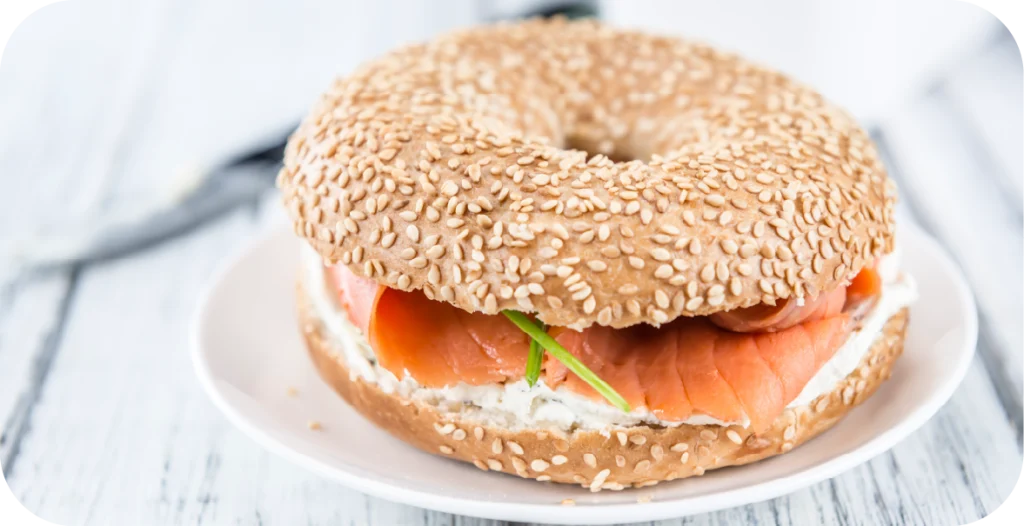 a bagel with smoked salmon, cream cheese and greens, covered in sesame seeds.