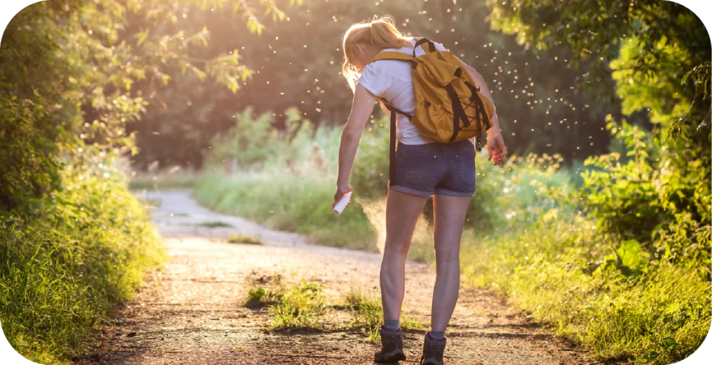 a young woman on a hiking trail applying bug spray to avoid vector-borne infection testing