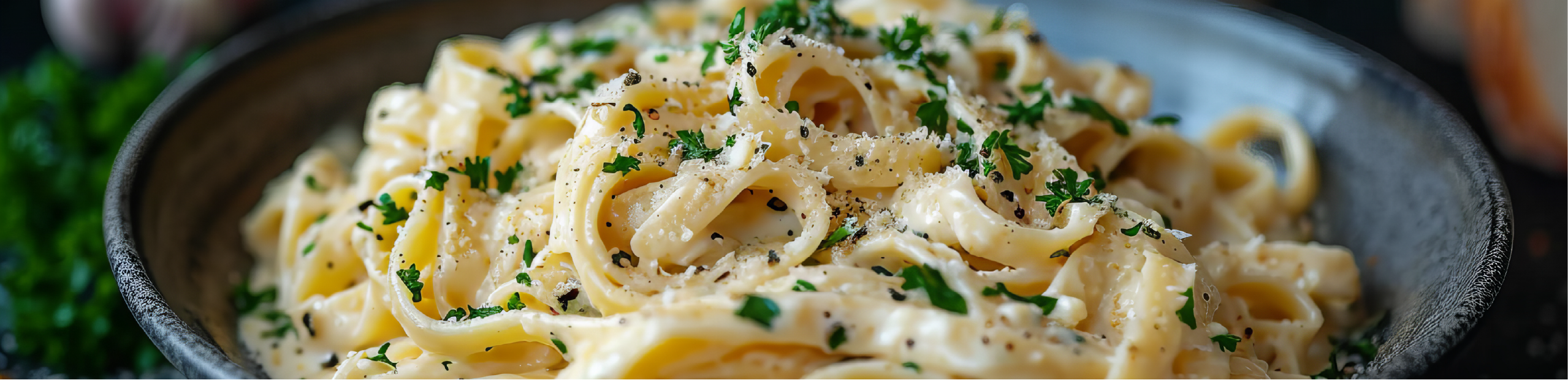 a bowl of alfredo pasta with chopped parsley and cracked pepper on top