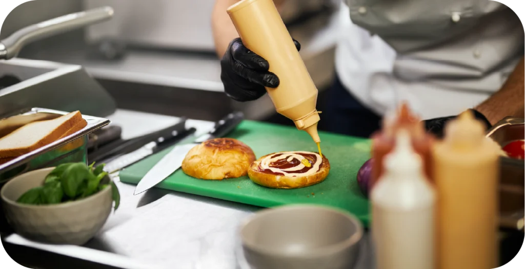 a man uses a squeeze bottle to apply sauce to a burger bun after food virus testing has been conducted