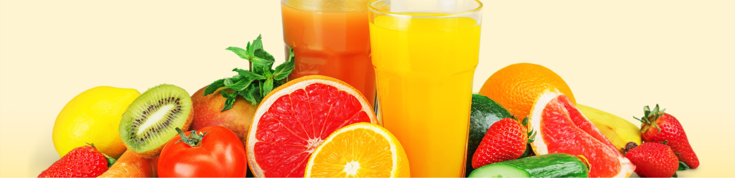 2 glasses of fruit juice surrounded by fresh fruits set on a yellow background