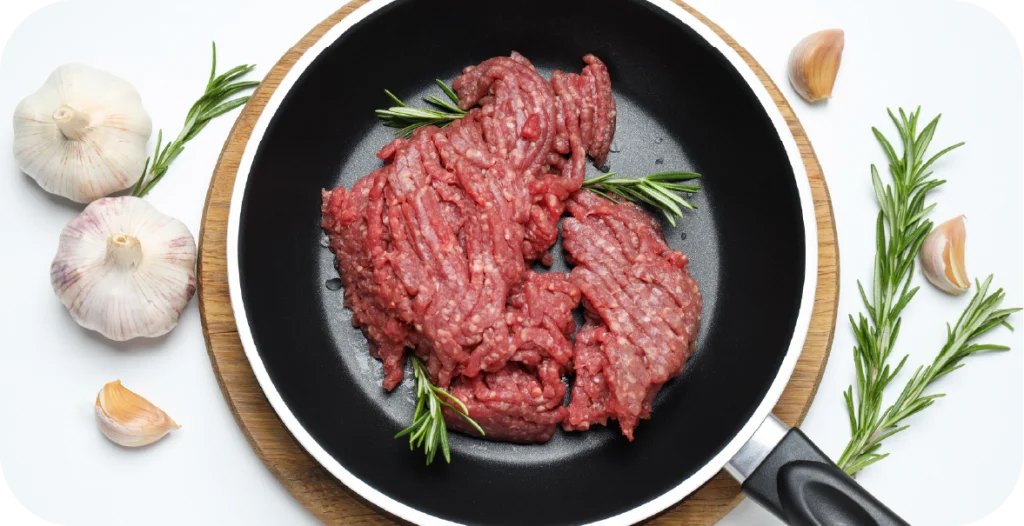 ground meat in a frying pan surrounded by garlic and rosemary