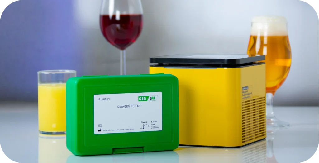 A RIDA®Cycler, a small yellow box with a black lid sits behind a cassette tray and its lid next to a test kit and some beverages