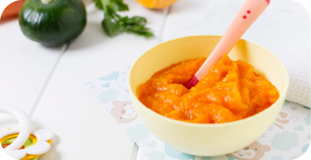 a bowl of baby food with a spoon on a white wooden table