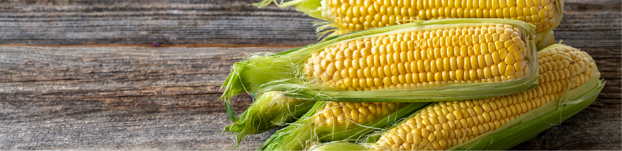 three ears of corn on a wooden table